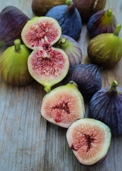 several green and deep purple figs with two cut in half, showing pink insides