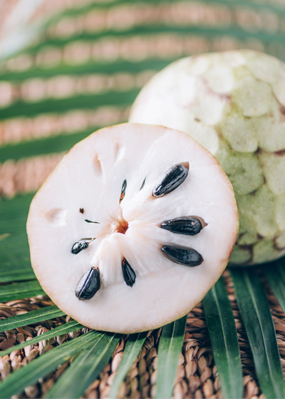Cherimoya fruit cut in half exposing off-white flesh and shiny black seeds